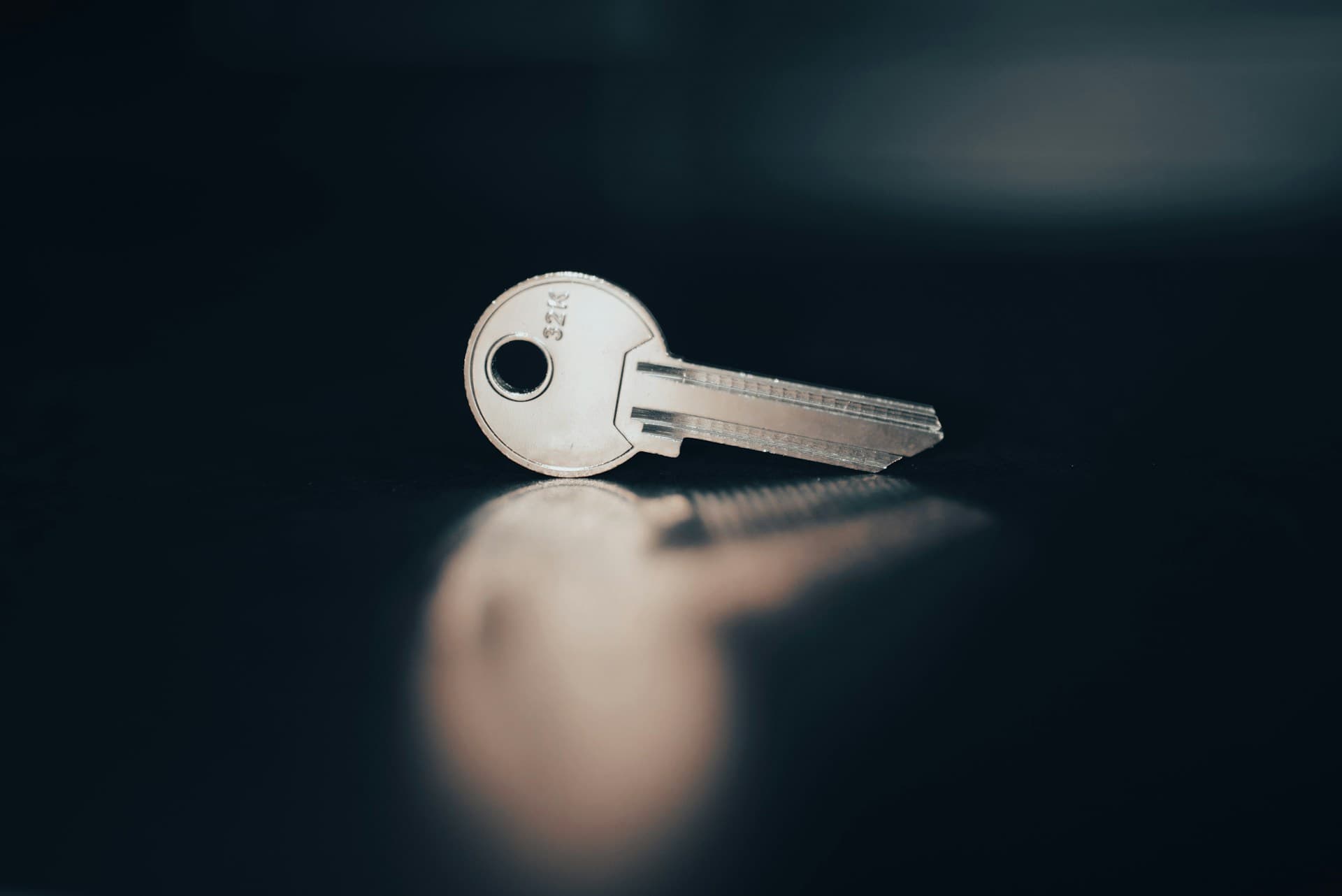 A close-up photograph of a single metal key resting on a dark reflective surface, with a soft, blurred background, used as a visual metaphor for access versus refresh tokens in authentication.